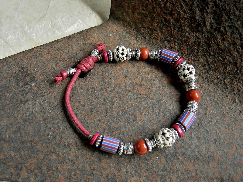 Adjustable slider bracelet in red, blue & white with Venetian glass, red jasper, carved bone & silver details. Red cotton cord.