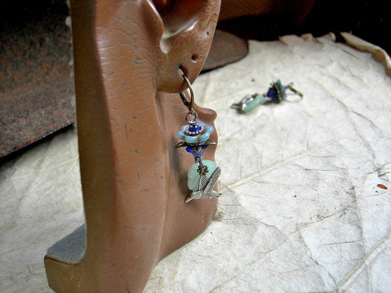 Silver hummingbird earrings with blue glass flowers, pale green glass leaf beads & antiqued brass and silver details.