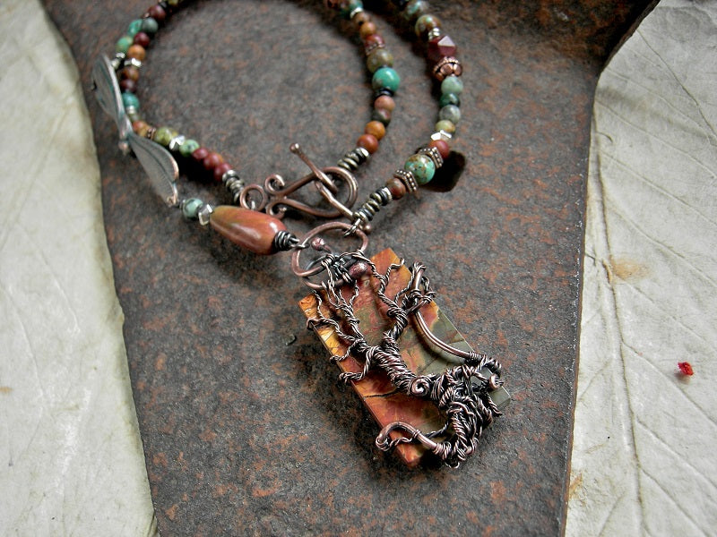 A strung bead necklace with Red Creek jasper & copper wire wrap tree focal, copper, jasper & turquoise beads & verdigris copper dragonfly connector.