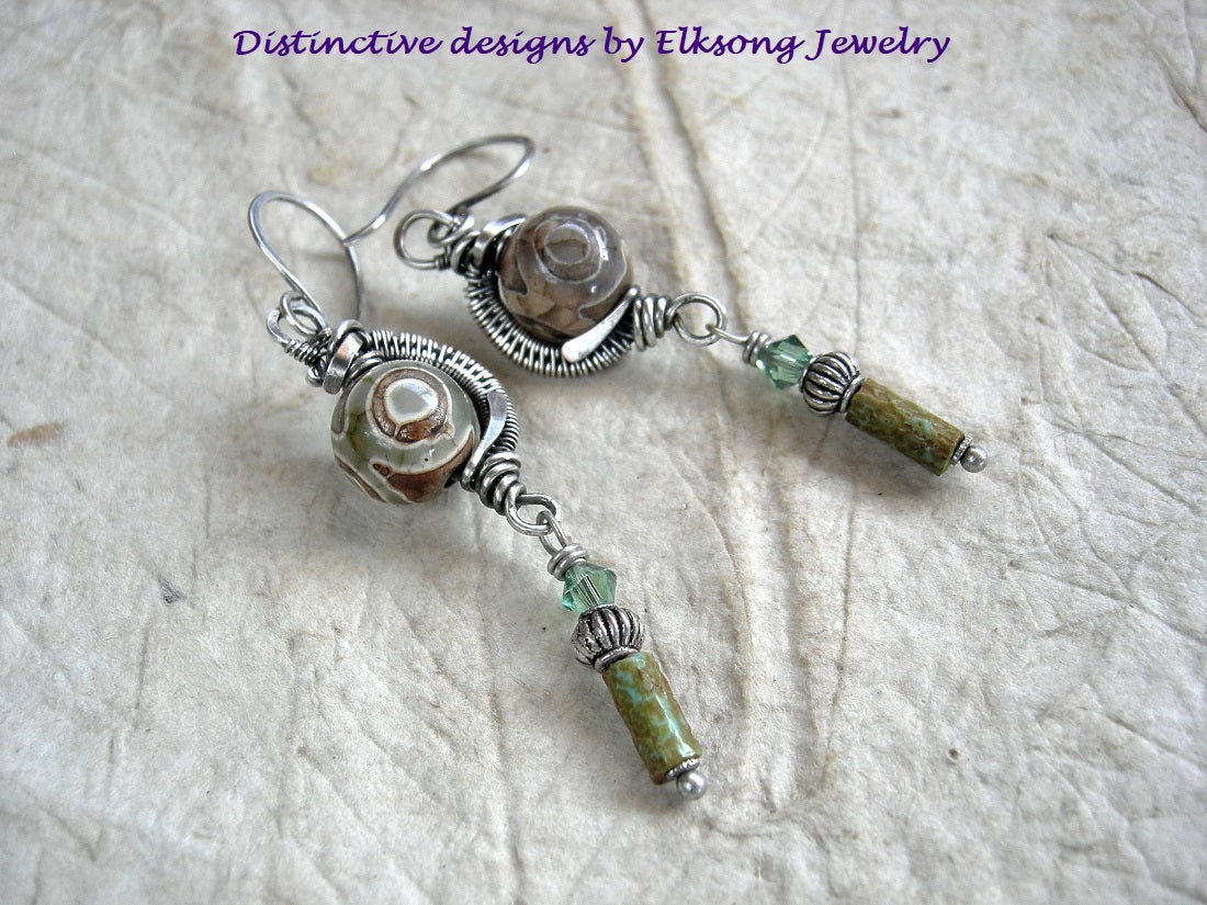Etched agate rounds in sterling wire wrap curves with green/brown glass cylinders, silver beads & green Swarovski crystals.