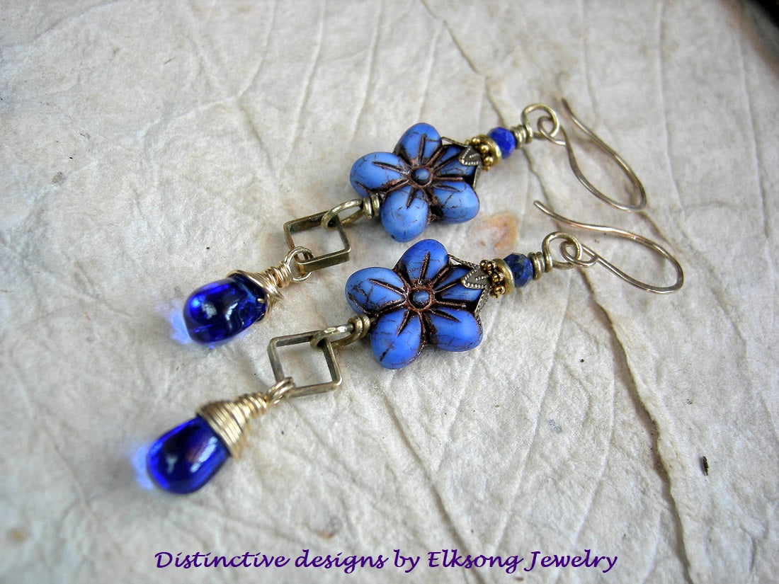 Blue flower-shaped earrings with gold accents, lapis gemstone & 14kt gf ear wires, branded 'Distinctive designs by Elksong Jewelry'.