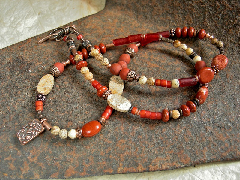 Asymmetrical strung bead wrap bracelet/necklace with red African glass cylinders & heishi, red & brown picture jasper, copper beads, toggle clasp & lotus charm. 