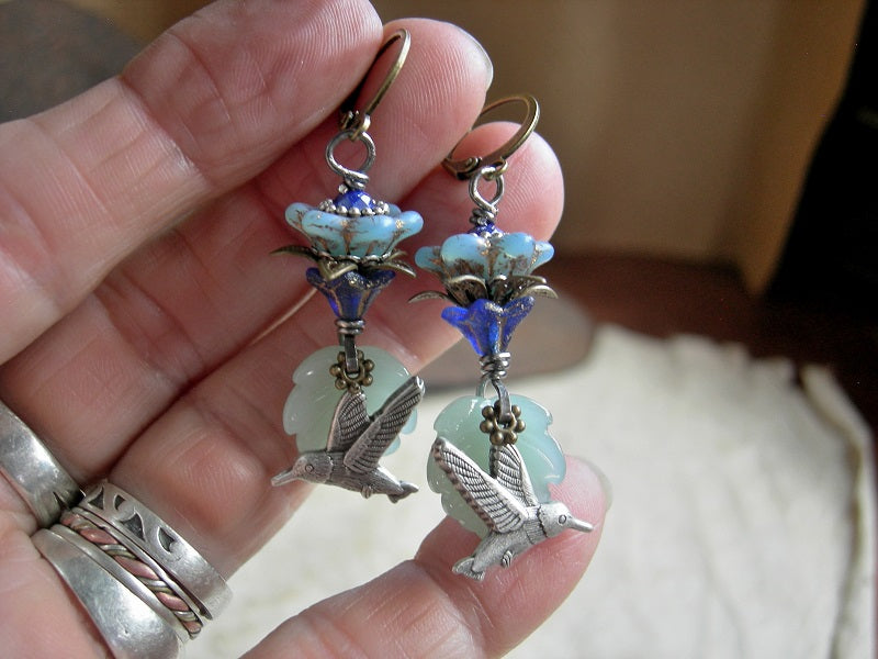 Nature inspired silver hummingbird earrings with blue glass flowers, pale green glass leaf beads & antiqued brass and silver details. 