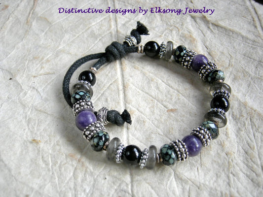Gothic theme adjustable slider bracelet with purple & black gemstone, black & grey glass and silver details. Black woven cotton cord.