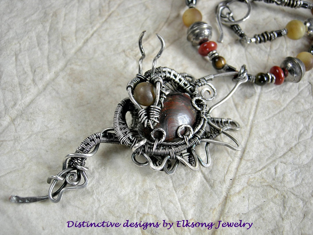 Silver dragon statement necklace with sterling wire wrap dragon & tiger iron cabochon focal. Strung red & gold gemstone, sterling bench bead necklace.