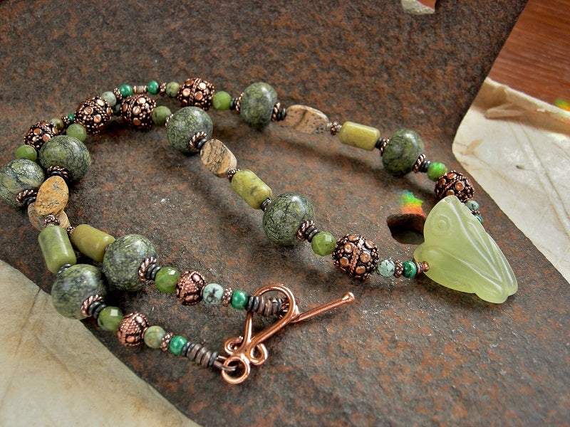 Strung bead style necklace with hand carved pale green serpentine frog focal, serpentine, jade, malachite,  jasper & copper beads. Copper toggle clasp. 