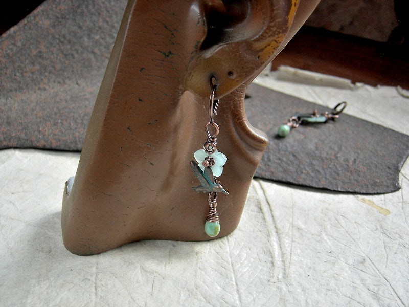 Nature inspired earrings with translucent pale green glass flowers, mint green glass tear drops & verdigris hummingbird charms. Lever back ear wires.