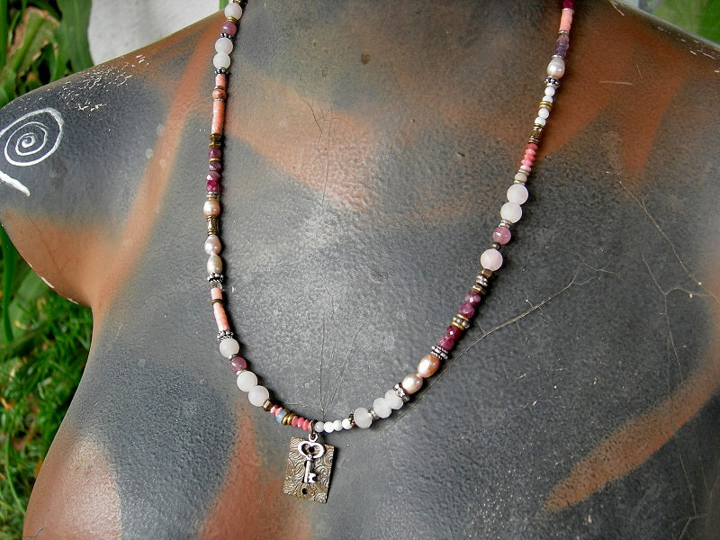 Pink strung bead necklace with rose quartz, pink coral, mother-of-pearl, freshwater pearl, red tourmaline & thulite gemstone beads, mixed silver & antiqued brass beads & focal. Adjustable sterling hook & eye clasp. 