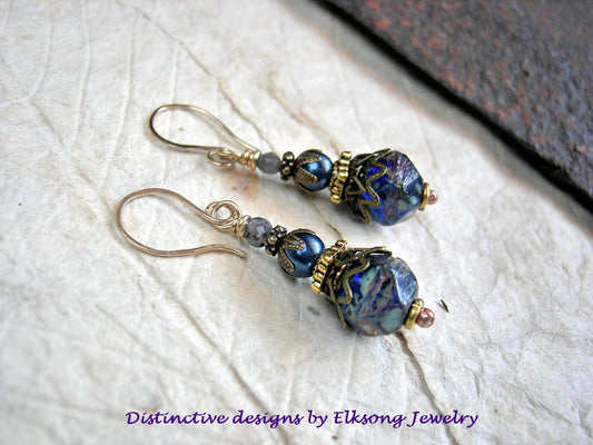 Pair of blue beaded earrings on a textured white surface with 'Distinctive designs by Elksong Jewelry' text.
