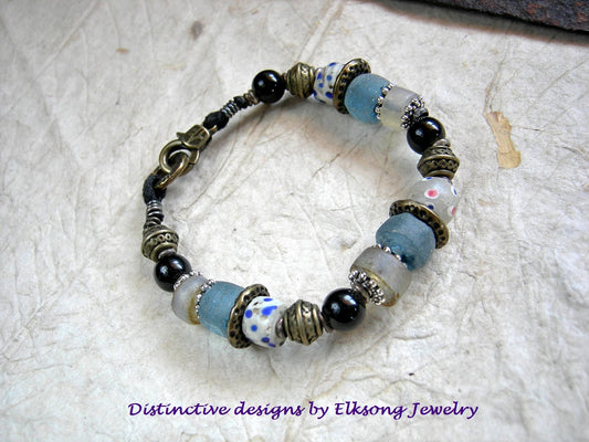 Beaded bracelet with blue, white and black beads & brass accents, featuring 'Distinctive designs by Elksong Jewelry'.