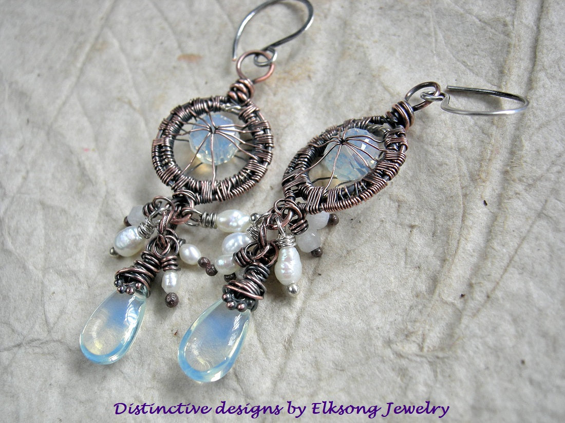 Pair of wire-wrapped earrings with opaline glass and pearls on a textured surface, branded 'Distinctive designs by Elksong Jewelry'.