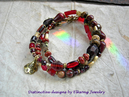 Beaded bracelet with red and gold accents on a textured surface, featuring 'Distinctive designs by Elksong Jewelry'.