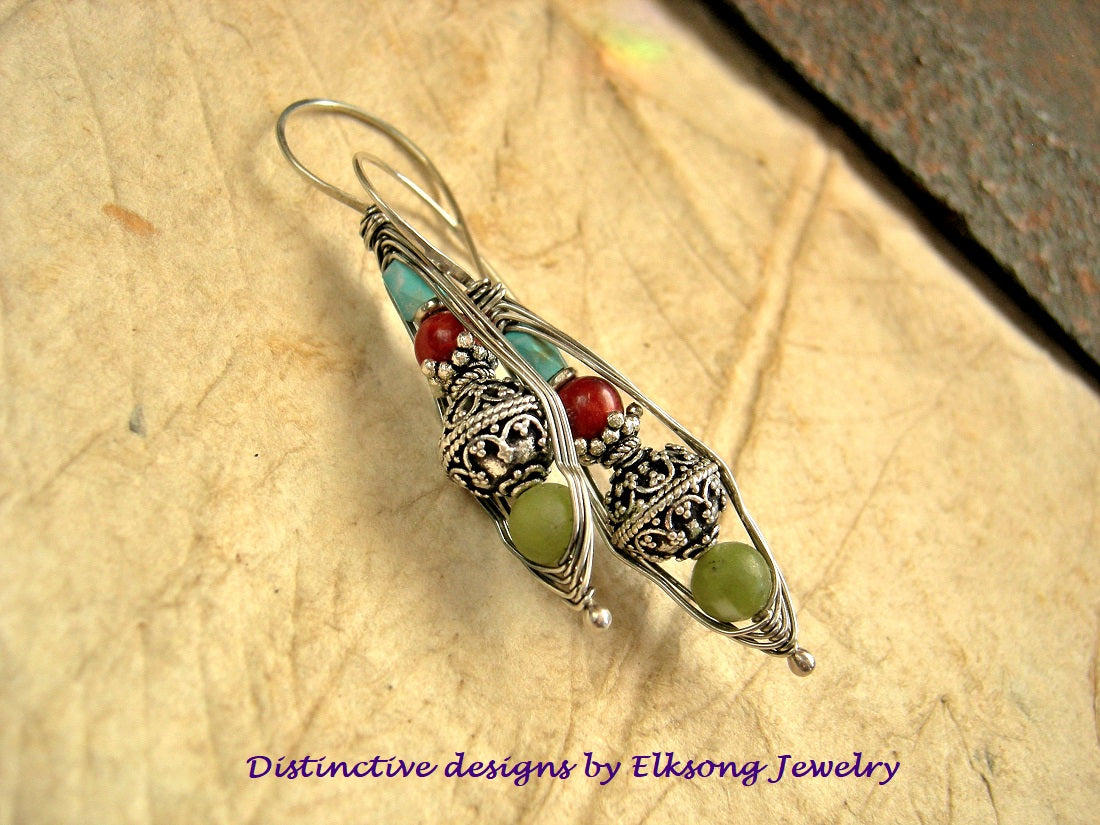 Silver earring with green and red beads on a textured surface, branded 'Distinctive designs by Elksong Jewelry'.