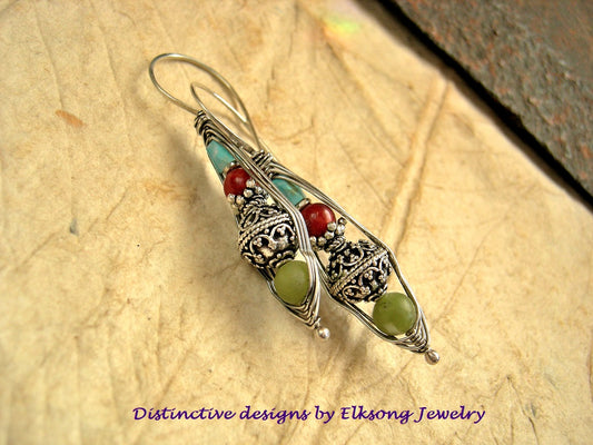 Silver earring with green and red beads on a textured surface, branded 'Distinctive designs by Elksong Jewelry'.