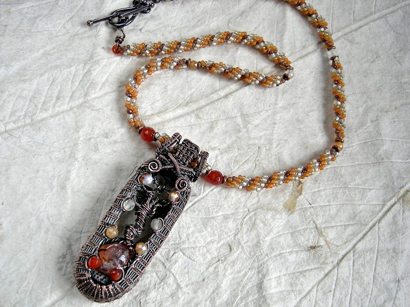 Art to wear copper tree art necklace with wire wrapped tree & faceted carnelian focal, woven seed bead rope necklace. Shades of orange & copper. 