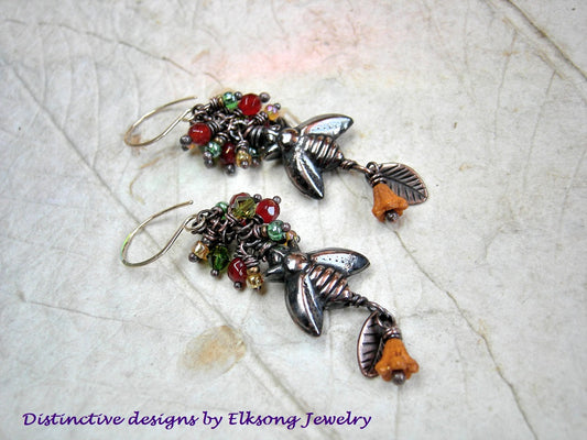 Orange & green cluster style earrings with oxidized copper bee beads, faceted carnelian, glass flowers & copper leaf charms. 